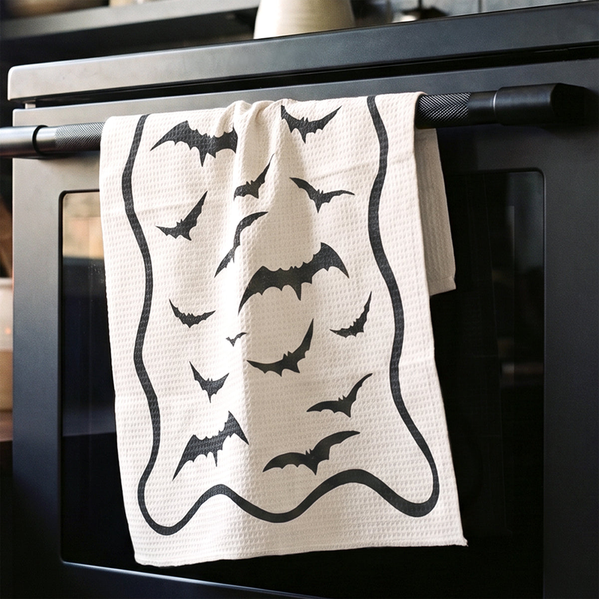 Bat Bash Halloween tea towel draped in kitchen setting, black bat print on cream linen by 723 & Co. Design Studio