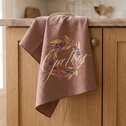 Gather watercolor autumn wreath tea towel by 723 & Co. Design Studio — gold leaves, mauve botanicals, and deep navy berries on warm mocha background with cream script lettering, microfiber kitchen linen printed from an original watercolor painting