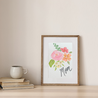 Custom watercolor floral painting with Mom name in frame next to books and coffee cup.
